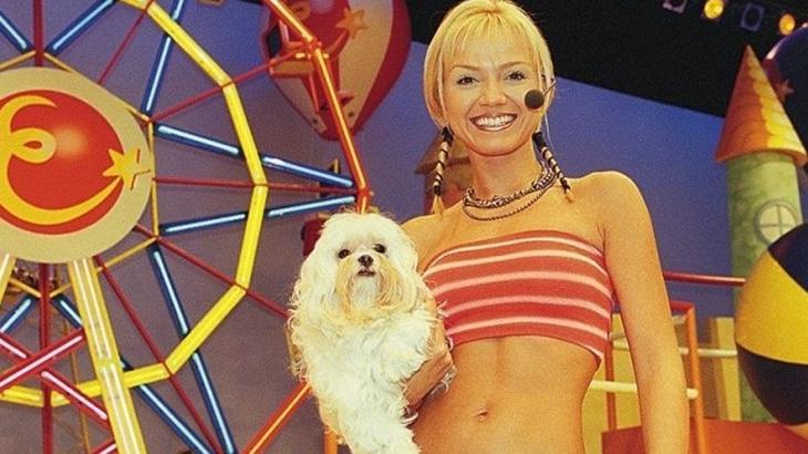 Apresentadora Eliana usando um top vermelho e segurando um cachorro branco de porte pequeno. Dia Mundial da Televisão. 