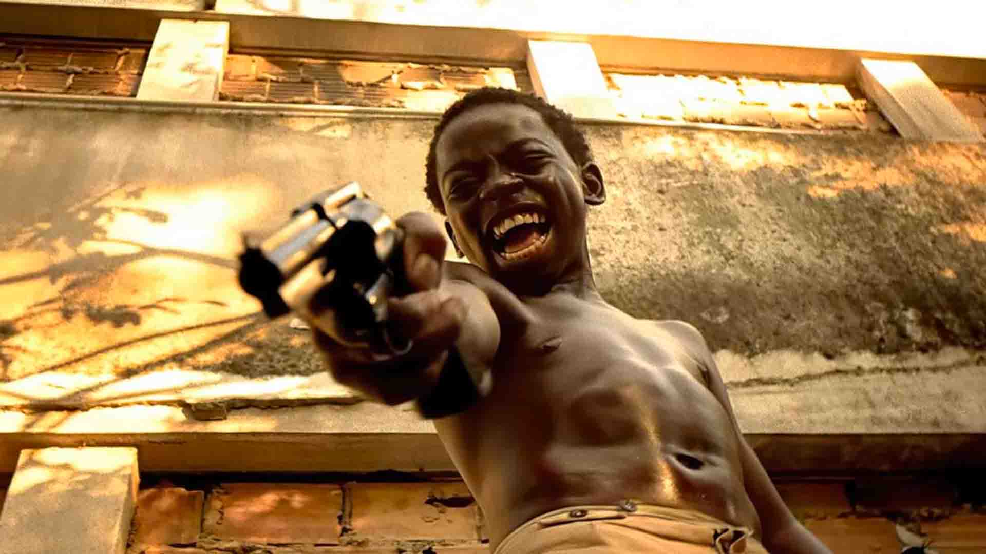 Cena do filme "Cidade de Deus", que mostra uma criança negra sem camisa segurando uma arma enquanto grita