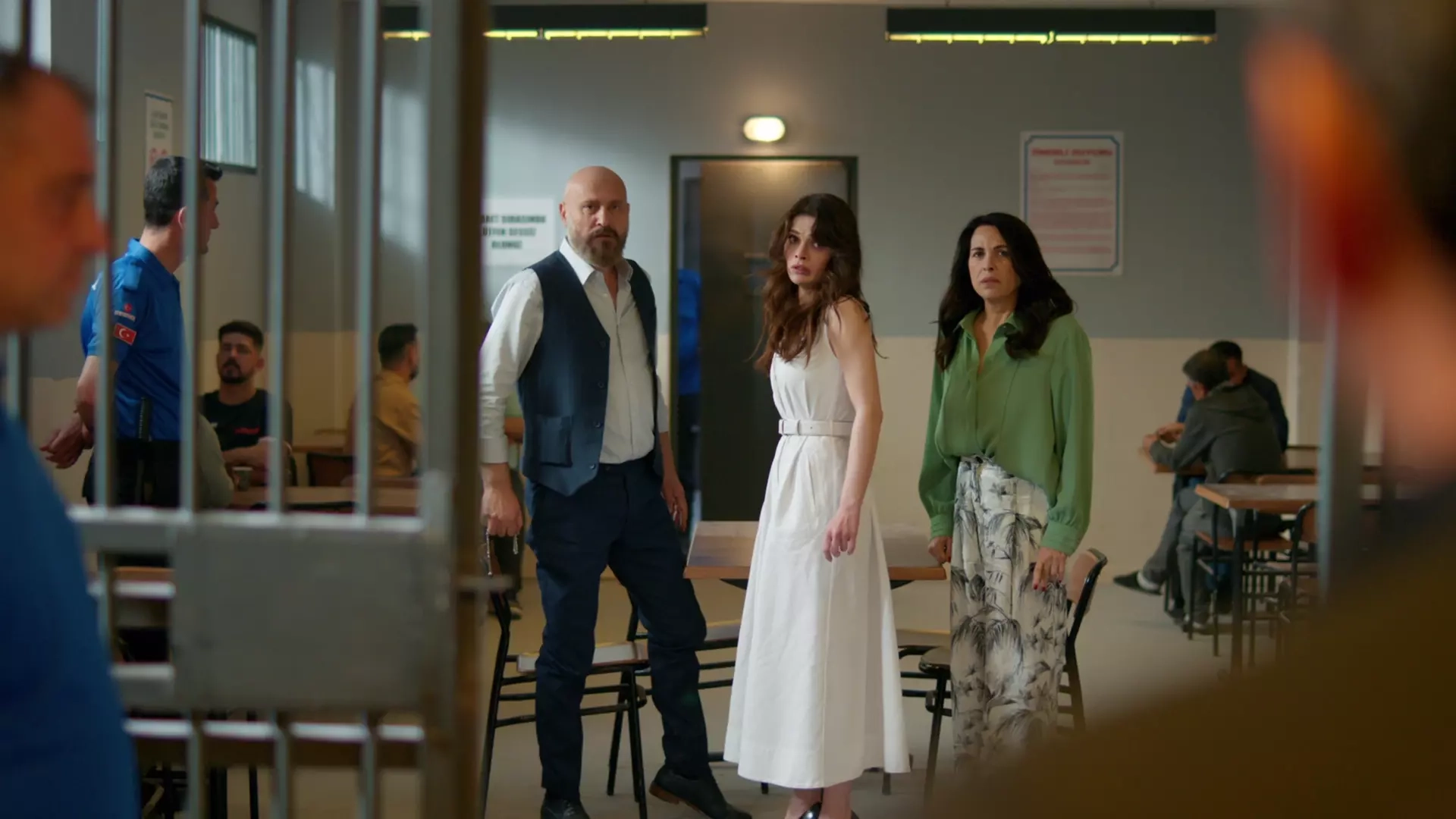 A foto mostra uma Cena de Uzak Şehir, novela turca, com duas mulheres e um homem visitando uma prisão