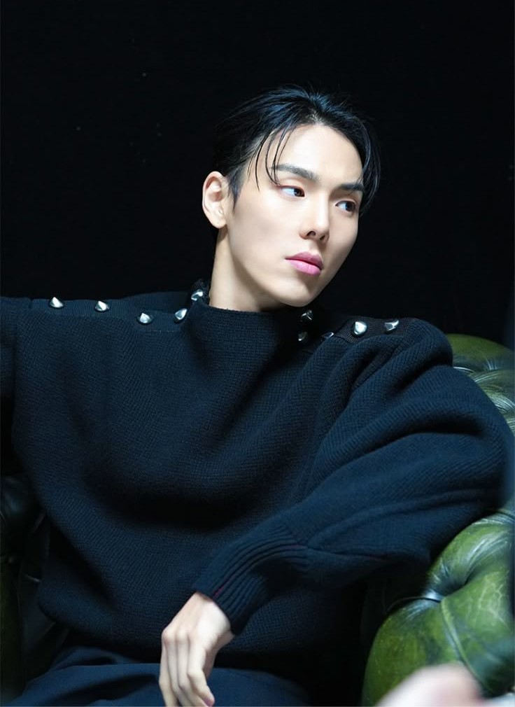 Shownu do MONSTA X sentado em uma poltrona verde olhando pro lado