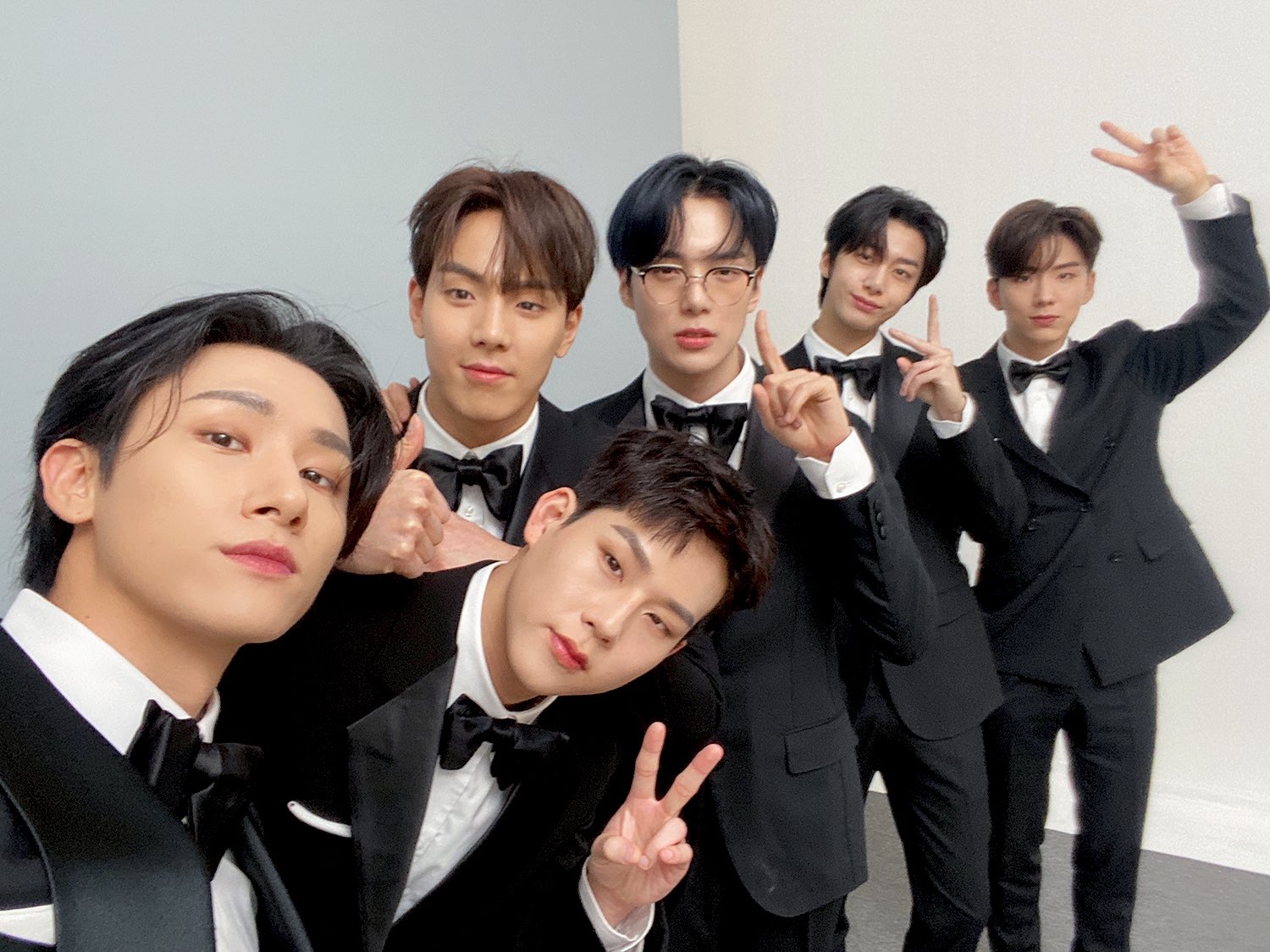 Integrantes do MONSTA X vestindo smoking prontos para participar de um programa