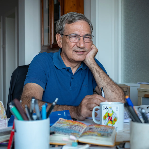 Orhan Pamuk em foto sentado na frente de uma mesa com cadernos e canetas