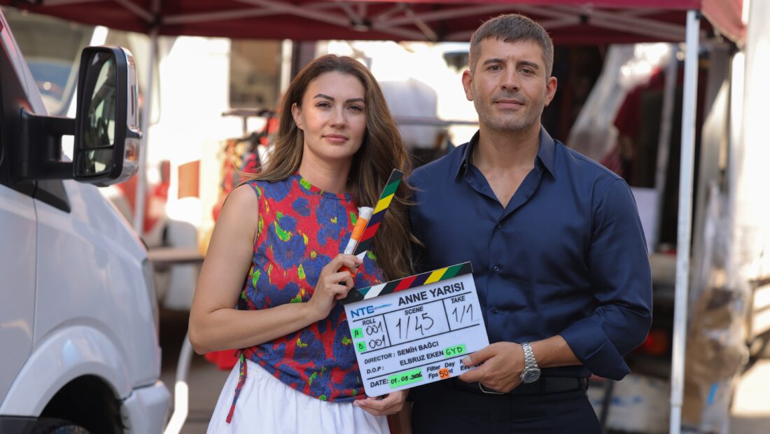 Cihangir Ceyhan e Burcu Özberk posam juntos durante as gravações de Anne Yarısı, segurando uma claquete diante de um veículo.