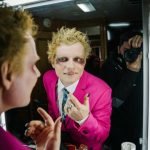 Ed Sheeran aparece em frente ao espelho. Ele está caracterizado como vampiro. Usa um terno rosa com uma camiseta social branca e gravata em tons frios. Atrás dele está um fotógrafo registrando esse momento. O fotógrafo está vestindo roupas pretas.