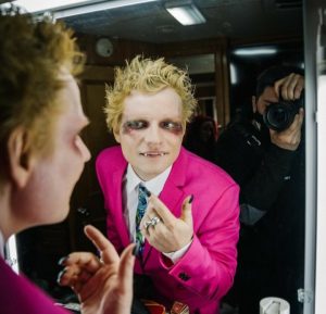 Ed Sheeran aparece em frente ao espelho. Ele está caracterizado como vampiro. Usa um terno rosa com uma camiseta social branca e gravata em tons frios. Atrás dele está um fotógrafo registrando esse momento. O fotógrafo está vestindo roupas pretas.