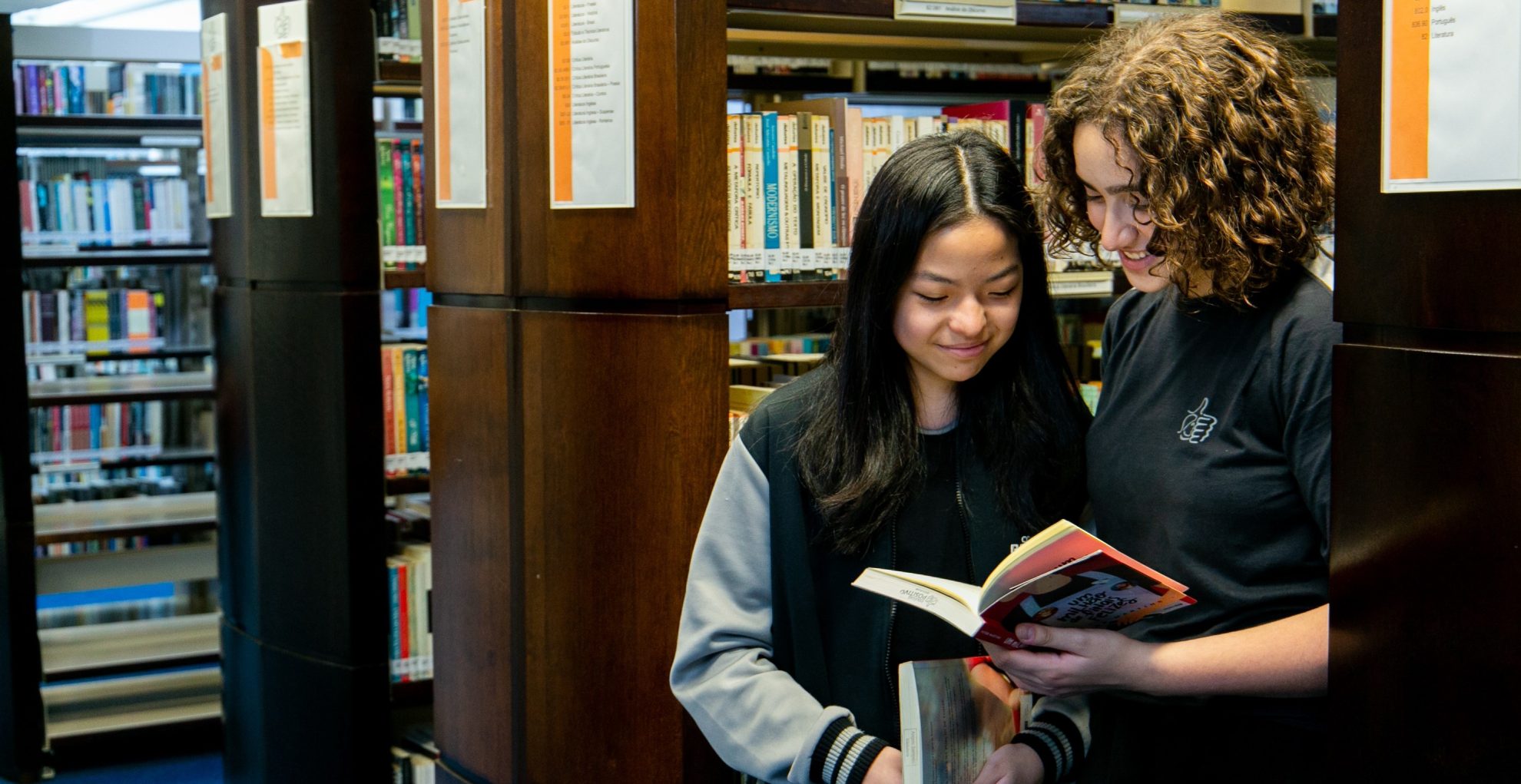 duas meninas olhando um livro em uma biblioteca