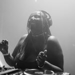 A imagem mostra a DJ Thais Queiroz tocando na noite