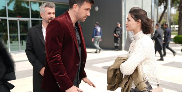 Kadir de terno vinho conversa com Meryem vestida de branco em frente a um edifício.