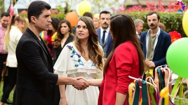 Faruk cumprimentando uma mulher, enquanto Süreyya olha para ele.