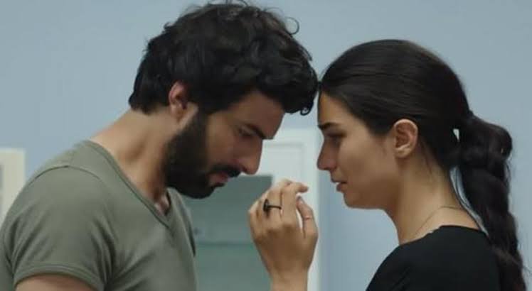 Engin Akyürek e Tuba Büyüküstün com o rosto próximos um dos outro em uma cena emocionante.