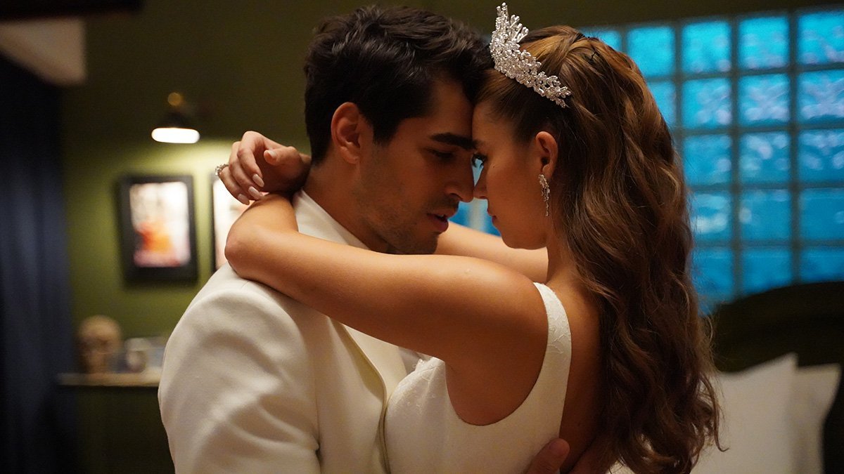 Seyran abraçada com Ferit. Ela usa um vestido de noiva branco e uma tiara na cabeça. Ele usa um terno branco.