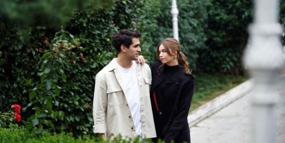 Seyran e Ferit caminham juntos por um jardim, trocando olhares.