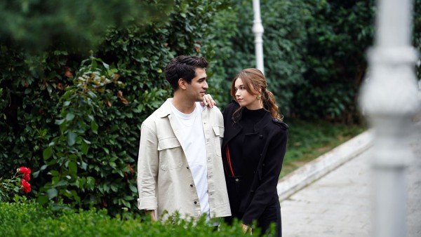 Seyran e Ferit caminham juntos por um jardim, trocando olhares.